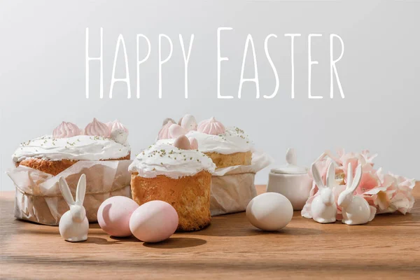 Декоративные кролики, куриные яйца, сахарная чаша, пасхальные торты и лепестки, изолированные на сером с счастливой пасхальной иллюстрацией — стоковое фото