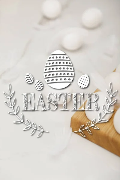 Foco seletivo de ovos em bandeja de ovos de madeira e penas em fundo branco com ilustração de Páscoa — Fotografia de Stock
