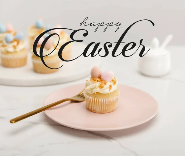 Enfoque selectivo de magdalenas en plato con tenedor y tabla redonda con azucarero sobre fondo gris con feliz ilustración de Pascua - foto de stock