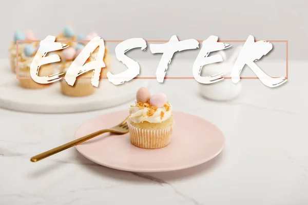 Selektiver Fokus von Cupcakes auf Teller mit Gabel und rundem Brett mit Zuckerdose auf grauem Hintergrund mit Osterillustration — Stock Photo