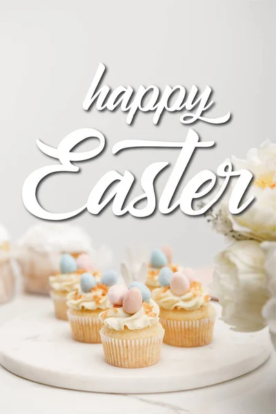 Mise au point sélective de cupcakes sur carton rond avec des fleurs sur fond gris avec illustration joyeuse de Pâques — Photo de stock