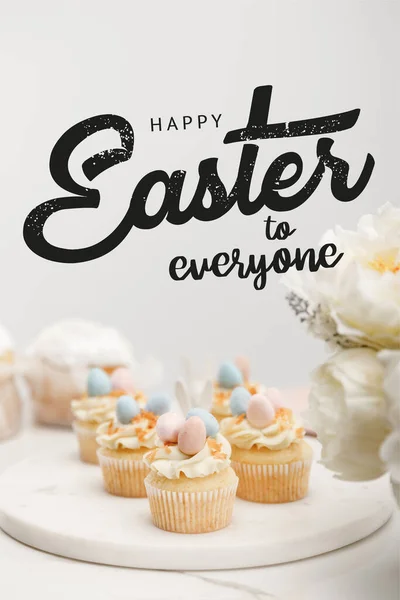 Selective focus of cupcakes on round board with flowers on grey background with happy Easter to everyone illustration — Stock Photo