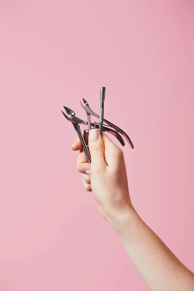 Vue recadrée de la main féminine avec poussoir à cuticules et pinces isolées sur rose — Photo de stock