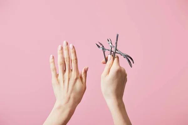 Vista recortada de la mujer sosteniendo empujador de cutícula y pinzas aisladas en rosa - foto de stock