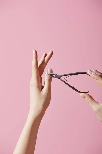 Vista parcial de la mujer haciendo manicura con pinza cutánea aislada en rosa - foto de stock