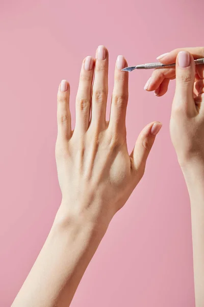 Partial view of woman doing manicure with cuticle pusher isolated on pink — Stock Photo