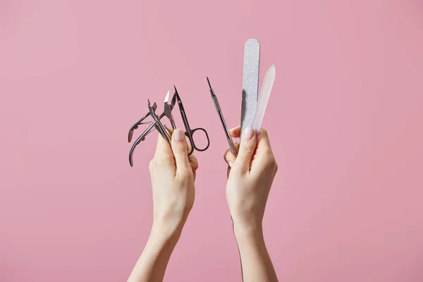 Vista recortada de la mujer sosteniendo instrumentos de manicura aislados en rosa - foto de stock