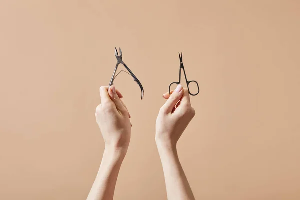 Cropped view of woman holding cuticle nipper and nail scissors isolated on beige — Stock Photo