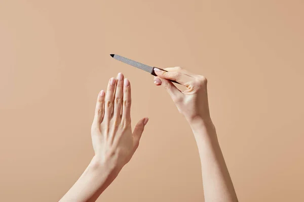 Vista cortada de mãos femininas com arquivo de unhas isolado no bege — Fotografia de Stock