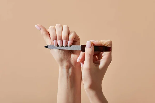 Vista recortada de la mujer limar las uñas aisladas en beige - foto de stock