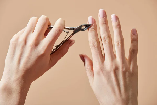 Vista recortada de la cutícula de corte de la mujer con pinza aislada en beige - foto de stock