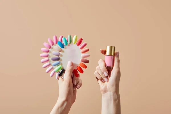 Vista recortada de la mujer sosteniendo botella y muestras de esmalte de uñas aislado en beige - foto de stock