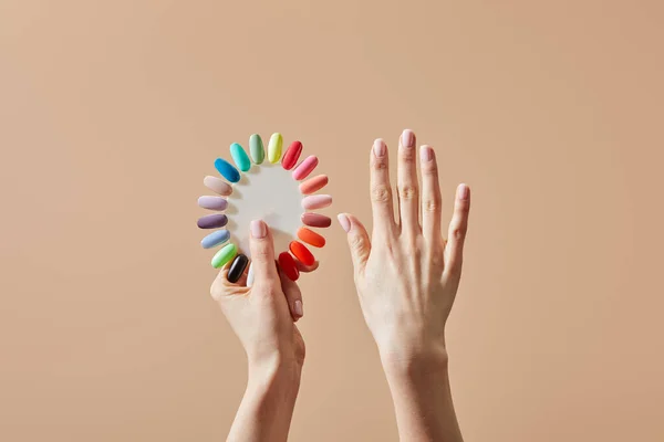 Partial view of woman holding multicolored samples of nail polish isolated on beige — Stock Photo