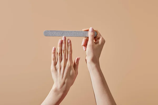 Cropped view of woman filing nail with emery board isolated on beige — Stock Photo