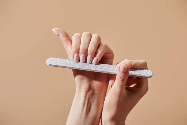 Cropped view of woman filing fingernails with emery board isolated on beige — Stock Photo