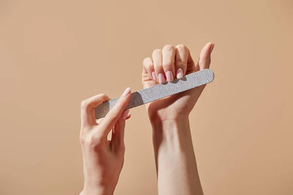 Partial view of woman filing fingernails with emery board isolated on beige — Stock Photo