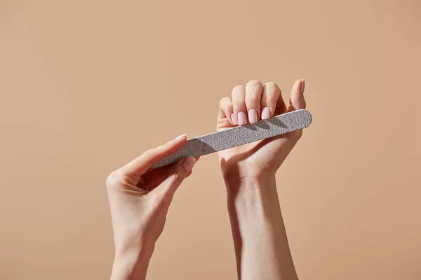 Partial view of woman filing nails with emery board isolated on beige — Stock Photo