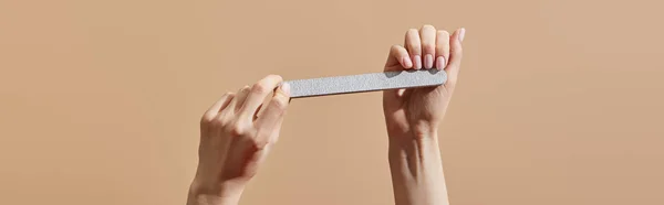 Partial view of woman filing nails with emery board isolated on beige, panoramic shot — Stock Photo