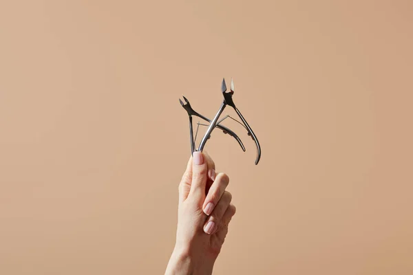 Vue partielle de la main féminine avec pinces à cuticules isolées sur beige — Photo de stock