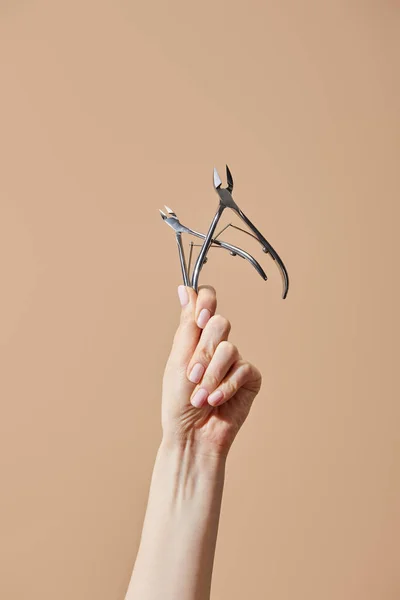 Cropped view of female hand with cuticle nippers isolated on beige — Stock Photo