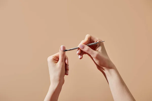 Vista recortada de la mujer haciendo manicura usando empujador de cutícula aislado en beige - foto de stock