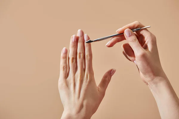 Partial view of woman doing manicure using cuticle pusher isolated on beige — Stock Photo