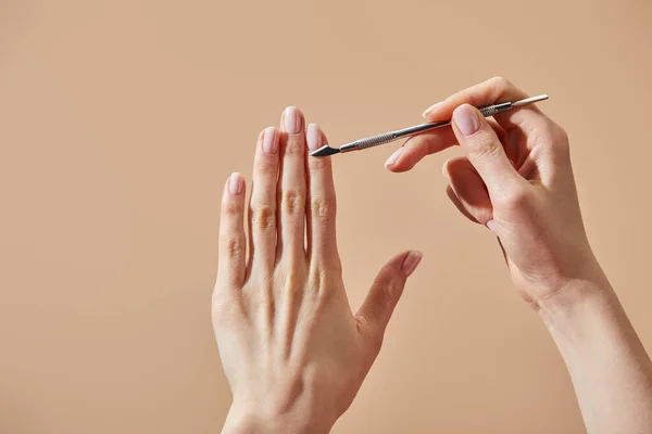 Partielle Ansicht der Frau bei Maniküre mit Nagelhautschieber isoliert auf beige — Stockfoto