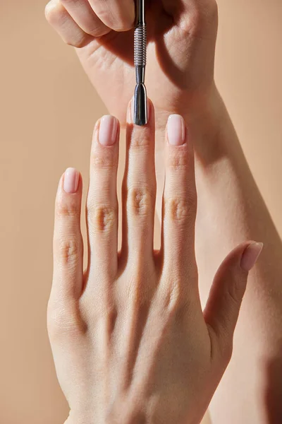 Partial view of woman doing manicure with cuticle pusher isolated on beige — Stock Photo