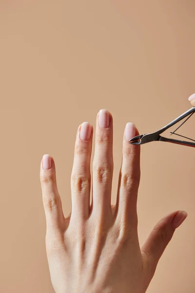 Partial view of woman doing manicure using cuticle nipper isolated on beige — Stock Photo