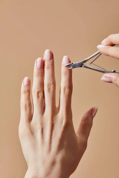 Partial view of woman using cuticle nipper isolated on beige — Stock Photo