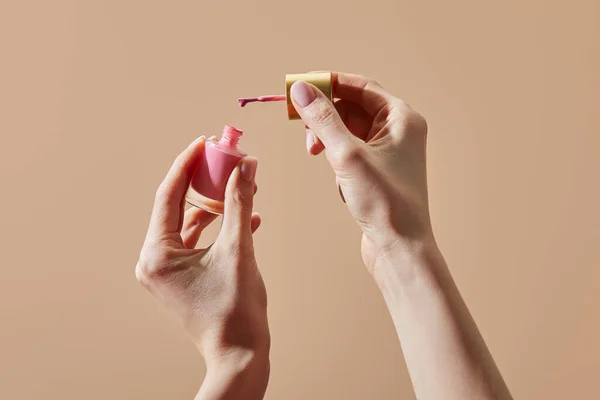 Частковий вигляд жінки, що тримає відкриту пляшку рожевого лаку для нігтів ізольовані на бежевому — стокове фото