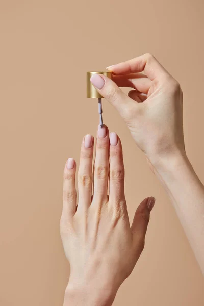 Частичный взгляд женщины, применяющей лак для ногтей изолирован от бежевого цвета — стоковое фото