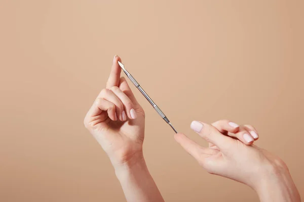 Partial view of female hands with cuticle pusher isolated on beige — Stock Photo