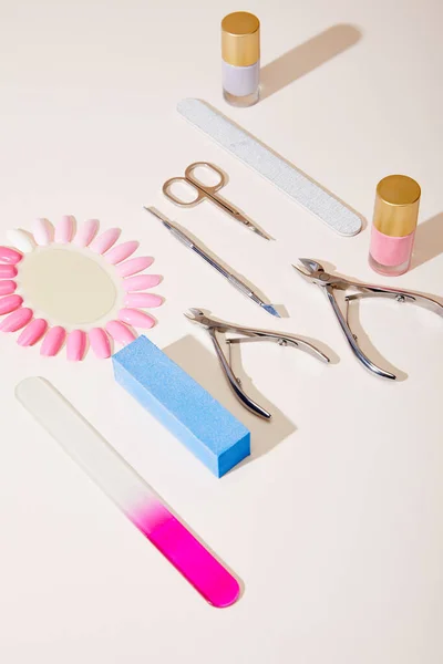 Vista de ángulo alto de muestras de esmalte de uñas con instrumentos de manicura sobre fondo blanco - foto de stock