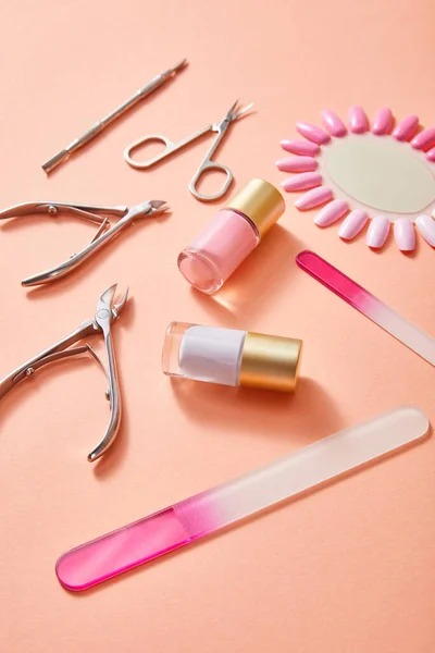 High angle view of bottles and samples of nail polish with manicure instruments on coral background — Stock Photo