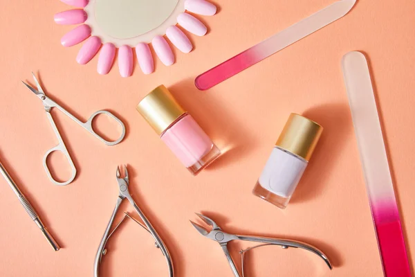 Top view of bottle and samples of nail polish with manicure instruments on coral background — Stock Photo