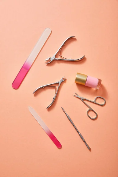 Top view of manicure instruments and bottle of pink nail polish on coral background — Stock Photo