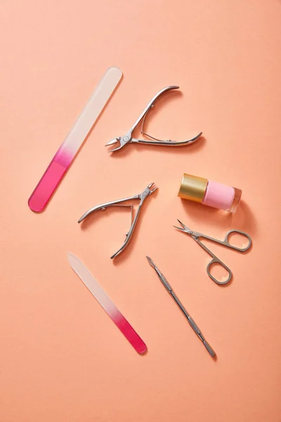 Vista dall'alto di strumenti di manicure e bottiglia di smalto rosa su sfondo corallo — Foto stock