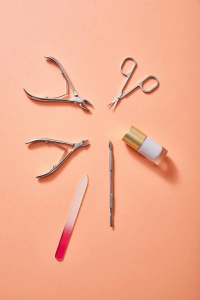 Top view of manicure instruments and bottle of white nail polish on coral background — Stock Photo