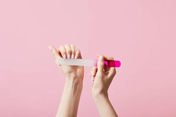 Vue recadrée de la femme faisant manucure à l'aide de lime à ongles isolée sur rose — Photo de stock