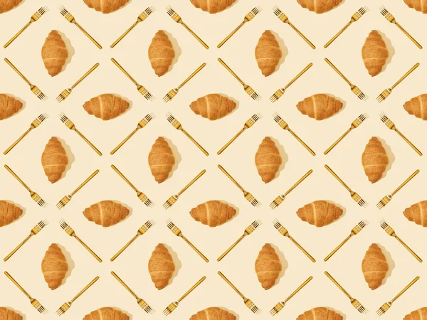 Vue de dessus des fourchettes et croissants dorés sur fond beige, motif sans couture — Photo de stock