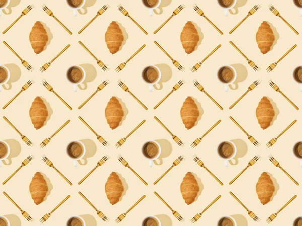 Вид зверху на золоті виделки, круасани та каву на бежевому, безшовному фоновому візерунку — стокове фото