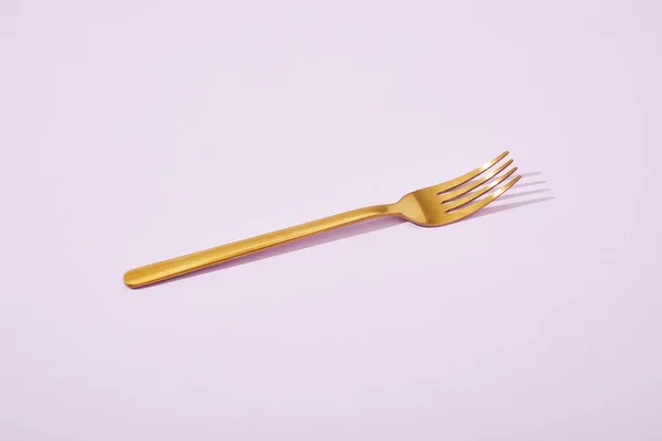Metal shiny golden fork on violet background — Stock Photo