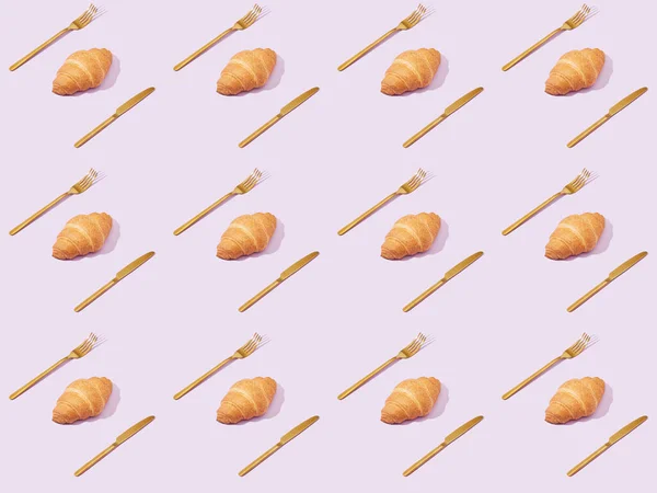 Goldene Gabeln und Messer mit Croissants isoliert auf violettem, nahtlosem Hintergrundmuster — Stockfoto