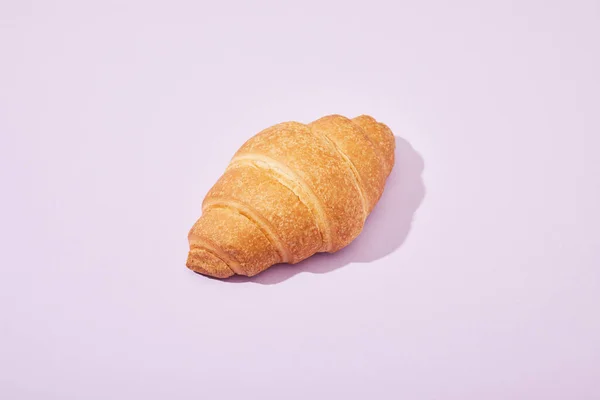 Croissant saboroso fresco no fundo violeta — Fotografia de Stock