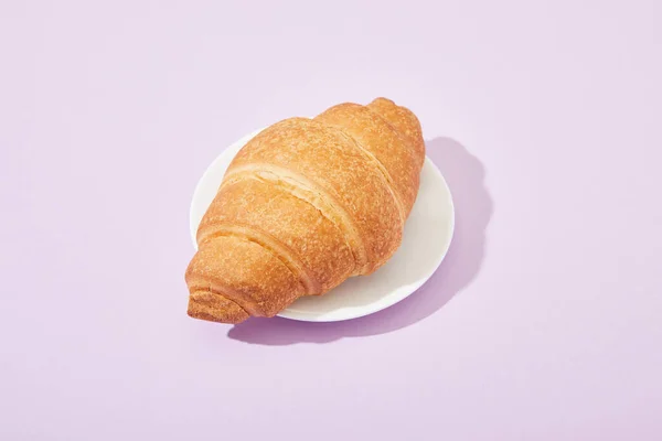 Fresh tasty croissant on plate on violet background — Stock Photo