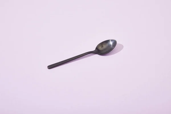 Metal shiny black spoon on violet background — Stock Photo