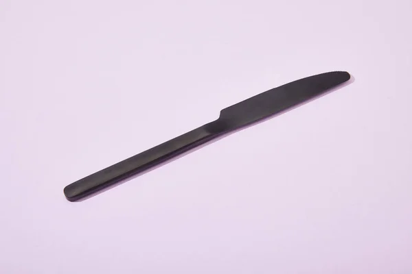 Metal shiny black knife on violet background — Stock Photo