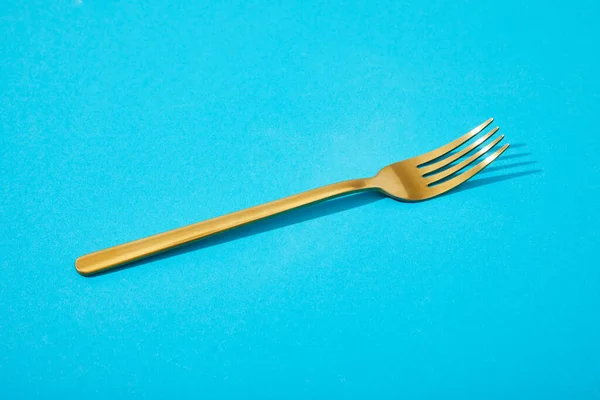 Metal shiny golden fork on blue background — Stock Photo