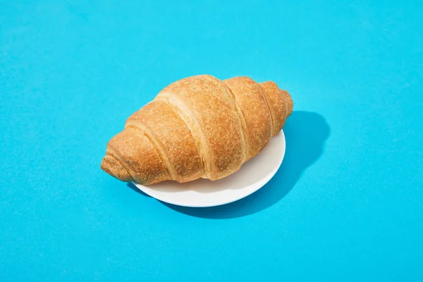 Frisches Croissant auf Teller auf blauem Hintergrund — Stockfoto